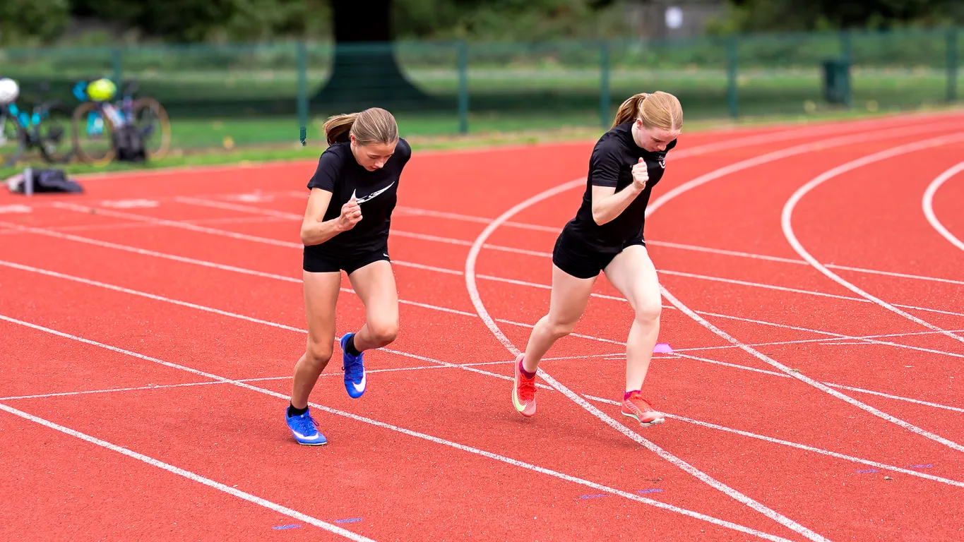 Two SpeedPro athletes in club training kit driving out of a standing start on the track
